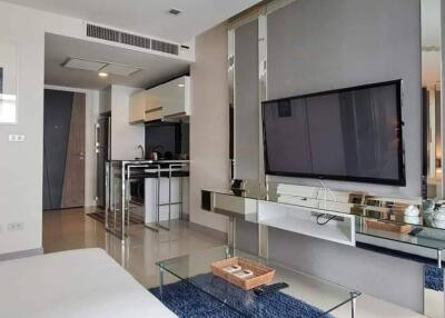 Modern living room with television, glass coffee table, and partial view of kitchen