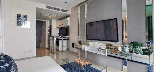 Modern living room with television, glass coffee table, and partial view of kitchen