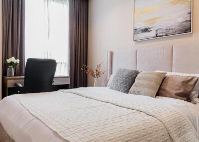 Modern bedroom with a large bed, window with curtains, desk with chair, and artwork on the wall