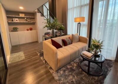 Modern living room with a sofa, glass table, bookshelves, and staircase