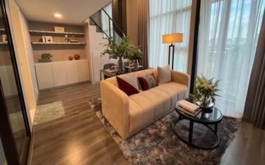 Modern living room with a sofa, glass table, bookshelves, and staircase