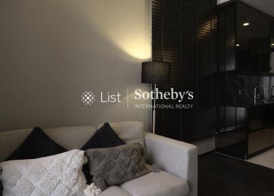 Modern living room with a cozy white sofa and black cushions, featuring a standing lamp and partial view of a sleek kitchen