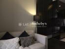 Modern living room with a cozy white sofa and black cushions, featuring a standing lamp and partial view of a sleek kitchen