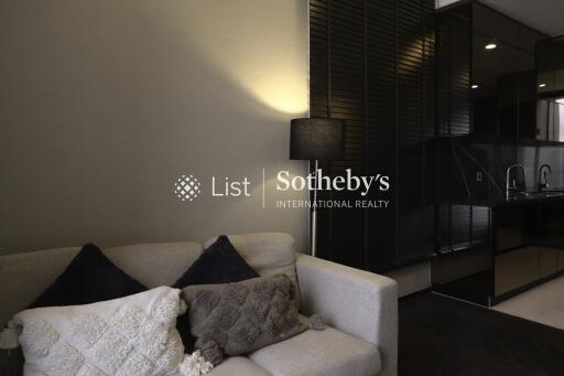 Modern living room with a cozy white sofa and black cushions, featuring a standing lamp and partial view of a sleek kitchen