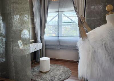 A modern bedroom with a vanity area, floor-to-ceiling windows, and a mannequin with a fur coat.