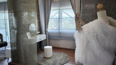 A modern bedroom with a vanity area, floor-to-ceiling windows, and a mannequin with a fur coat.