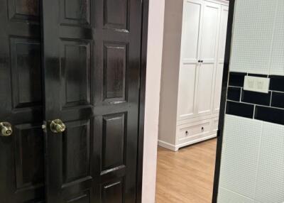 View of a room with dark double doors and wooden floor leading to a bright hallway with a white cabinet