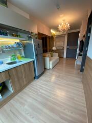 Modern kitchen area with a view into the living space, featuring wood flooring, stainless steel appliances, and a chandelier.