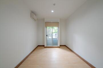 Spacious empty room with wooden flooring, large window, and air conditioning