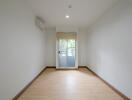 Spacious empty room with wooden flooring, large window, and air conditioning