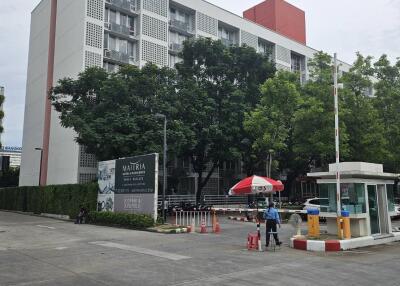 Exterior view of a residential building with security post and surrounding trees