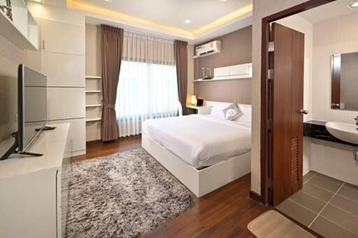 Modern bedroom with hardwood floors, large bed, and en-suite bathroom