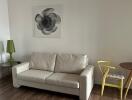 Living room with beige sofa, green lamp, yellow chair, and wall art