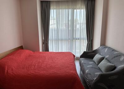 Bedroom with large window, red bedspread, and grey sofa