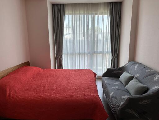 Bedroom with large window, red bedspread, and grey sofa