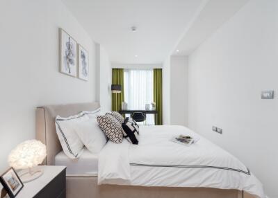 Modern bedroom with double bed, nightstand, wall art, and workspace in the background