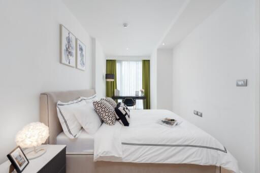 Modern bedroom with double bed, nightstand, wall art, and workspace in the background