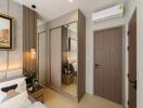 A well-decorated bedroom with modern furnishings, a mirrored wardrobe, and air conditioning.