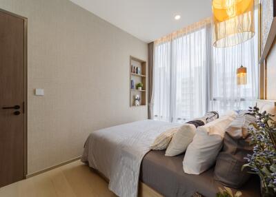 Cozy bedroom with a neatly made bed, built-in shelves, and large windows with sheer curtains