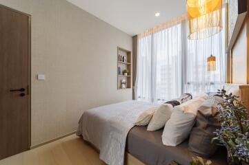 Cozy bedroom with a neatly made bed, built-in shelves, and large windows with sheer curtains