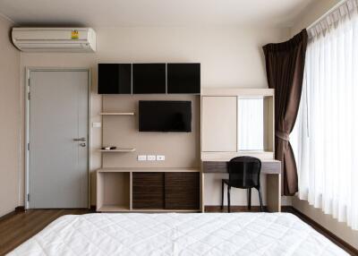 Modern bedroom with a wall-mounted TV, air conditioning unit, and desk