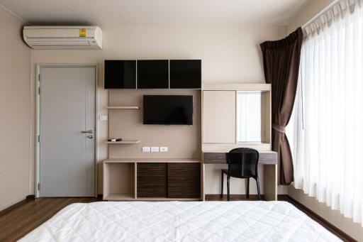 Modern bedroom with a wall-mounted TV, air conditioning unit, and desk