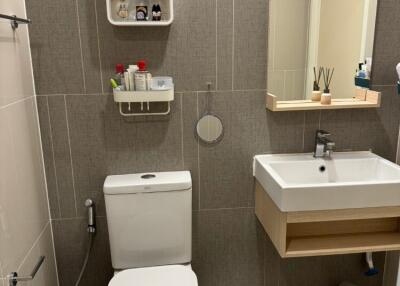 A modern bathroom with a sink, wall-mounted mirror, toilet, and shelf with toiletries