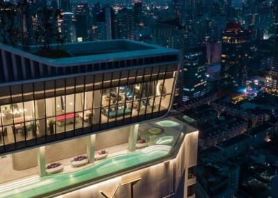 Exterior view of a high-rise building with rooftop swimming pools and cityscape at night