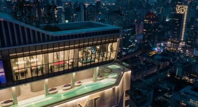 Exterior view of a high-rise building with rooftop swimming pools and cityscape at night