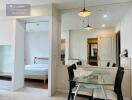 Dining area adjacent to a room with bed, glass table with chairs, and mirror wall.