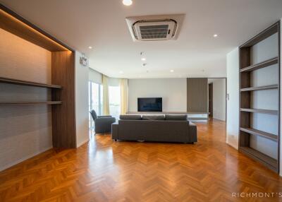 Spacious living room with wooden flooring, built-in shelves, and large windows