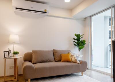 Modern living room with a beige sofa, air conditioner, lamp, and indoor plant