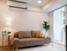 Modern living room with a beige sofa, air conditioner, lamp, and indoor plant