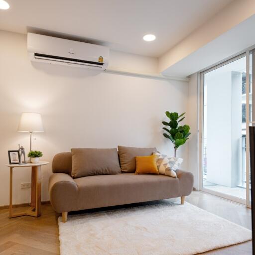 Modern living room with a beige sofa, air conditioner, lamp, and indoor plant