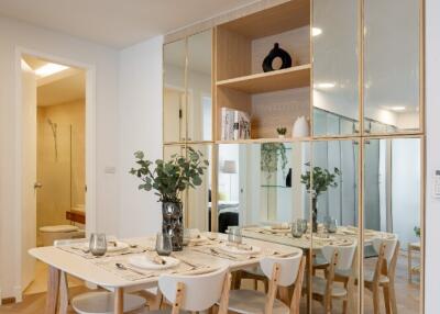 Modern dining area with wooden table and chairs, adjacent to decorated shelves and mirrored wall