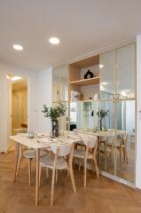 Modern dining area with wooden table and chairs, adjacent to decorated shelves and mirrored wall