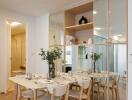 Modern dining area with wooden table and chairs, adjacent to decorated shelves and mirrored wall