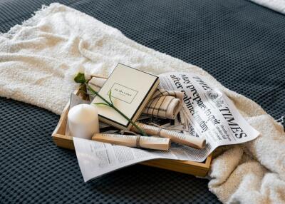 Bed with a neatly arranged tray containing a book, a candle, a flower, and a newspaper