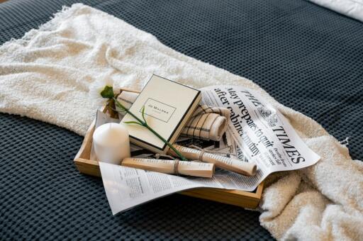 Bed with a neatly arranged tray containing a book, a candle, a flower, and a newspaper