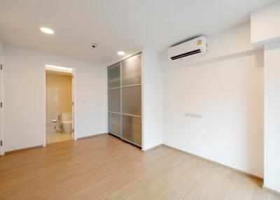 Empty bedroom with wooden flooring, air conditioning, sliding closet doors, and view of an attached bathroom.