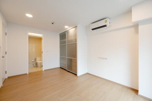 Empty bedroom with wooden flooring, air conditioning, sliding closet doors, and view of an attached bathroom.