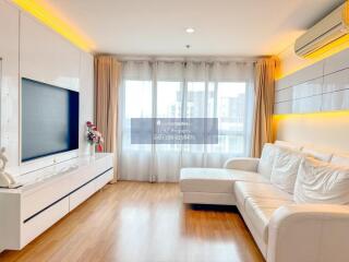 Modern living room with white furniture, wooden flooring, and large windows