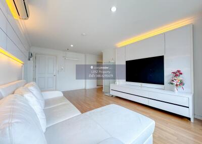 Spacious and modern living room with large white sofa, wooden flooring, and flat-screen TV