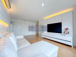 Spacious and modern living room with large white sofa, wooden flooring, and flat-screen TV