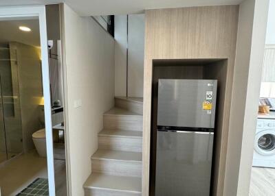 Compact modern kitchen area with fridge, beside staircase and adjacent bathroom