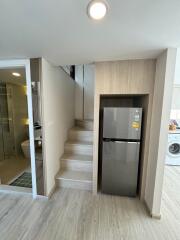 Compact modern kitchen area with fridge, beside staircase and adjacent bathroom