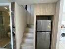 Compact modern kitchen area with fridge, beside staircase and adjacent bathroom