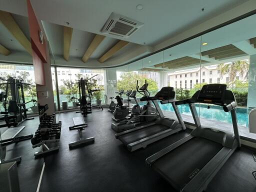 Well-equipped fitness center with various exercise machines and a view of the pool