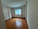 Empty bedroom with wooden floor and a window with curtains