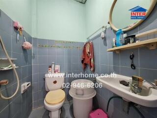 A compact bathroom with toilet, sink, and a variety of toiletries